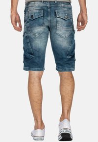 Pantaloni cargo in denim blu sbiadito con più tasche, dettagli cuciti e taglio dritto, abbinati a sneakers bianche.