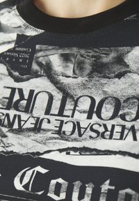Juodos trumpomis rankovėmis marškinėliai su monochrominių grafikų koliažu, kuriame yra susidėvėjusių tekstų ir tekstūrų. Juoda gipiūrinė apykaklė.