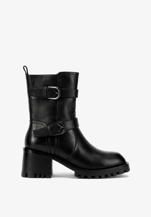 Schwarze Lederstiefelette mit zwei verstellbaren Riemen und silbernen Schnallen, einem klobigen Absatz und einer strukturierten Gummisohle.