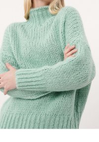 Mintgrön, tjockstickad tröja med hög hals, ribbade muddarna och lös passform. Mjuk textur med synliga sömnadsmönster.