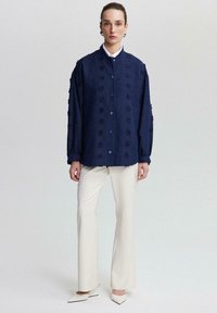 Navy embroidered button-up shirt with textured floral details, paired with cream wide-leg trousers and pointed-toe mules.
