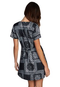 Robe noire à manches courtes avec des motifs blancs complexes de paisley et géométriques, taille cintrée avec un détail noué, texture de tissu douce.