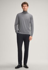 Gray turtleneck sweater, knit texture, paired with slim-fit navy trousers and black shoes. Model stands against a light gray background.