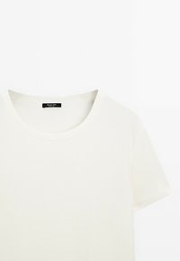 T-shirt a maniche corte color crema chiaro con scollatura rotonda. Texture liscia, design minimalista, con un'etichetta nera sul collo.