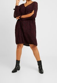 Rot-schwarz gestreiftes Kleid mit V-Ausschnitt, langen Ärmeln und Cut-out-Details. Kombiniert mit schwarzen Stiefeletten.