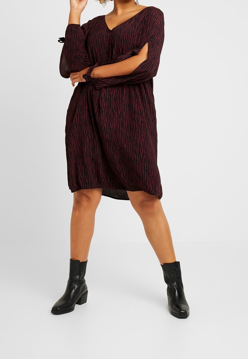 Rot-schwarz gestreiftes Kleid mit V-Ausschnitt, langen Ärmeln und Cut-out-Details. Kombiniert mit schwarzen Stiefeletten.