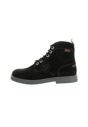 Botín de ante negro hasta el tobillo con cordones en la parte delantera, suela de goma y costuras blancas. Cuenta con una etiqueta de marca y un lazo en el talón.