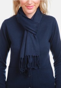 Écharpe tricotée bleu foncé aux bords frangés, confectionnée dans un matériau doux, enroulée autour du cou, complétant un pull assorti.