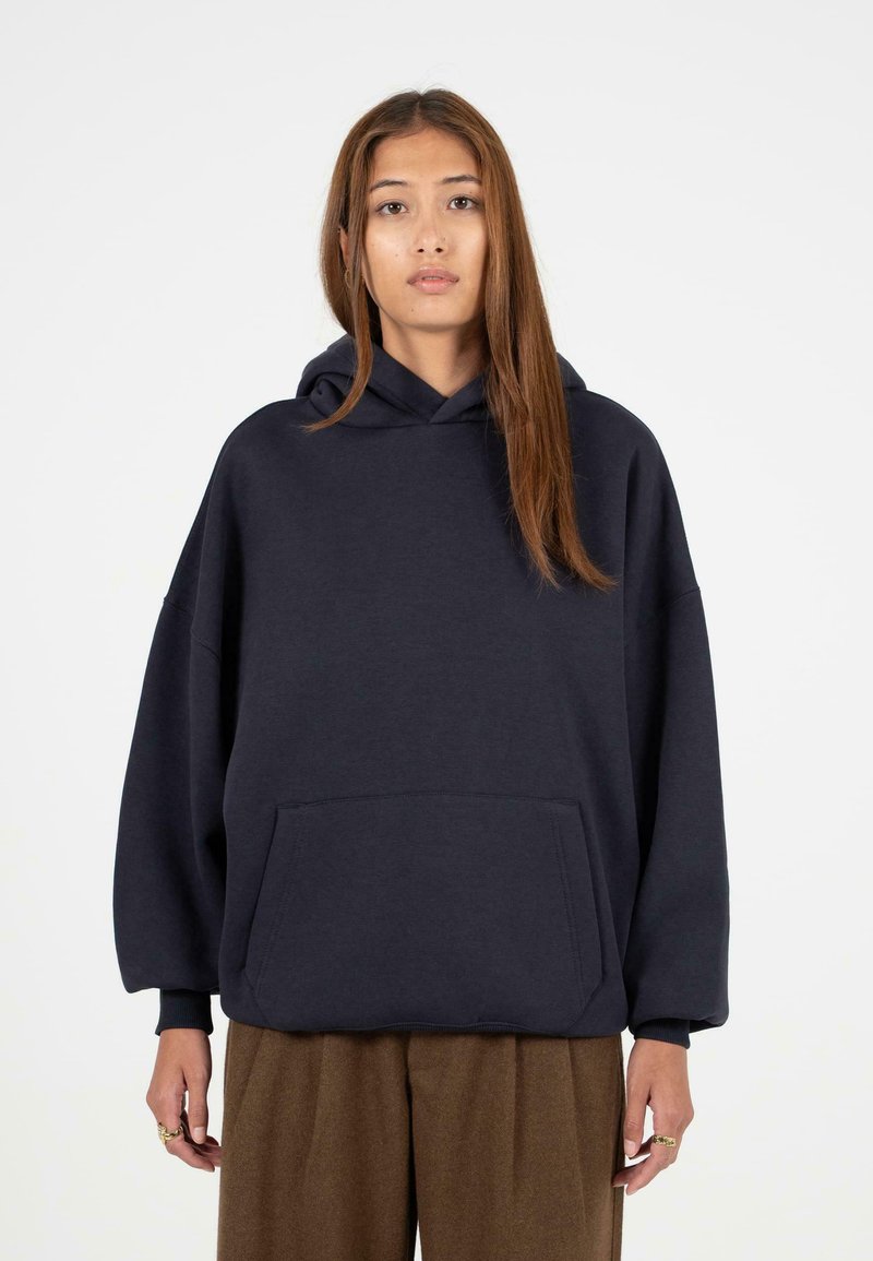 Marineblauwe oversized hoodie van zachte stof, met een kangoeroezak en geribbelde manchetten. Eenvoudig ontwerp zonder zichtbare patronen.