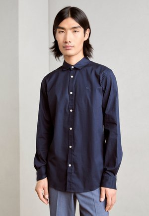 Marineblauwe langekorte mouw shirt met een kraag met knopen, voorknopen en een subtiel logo op de borst. De stof lijkt glad en gestructureerd.