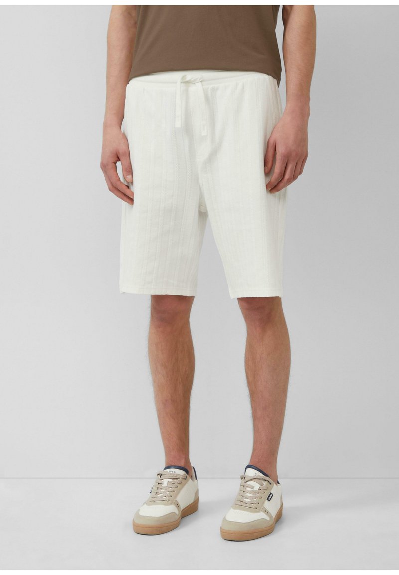 Weiße, strukturierte Shorts mit einem geriffelten Muster, ausgestattet mit einem Kordelzugbund und seitlichen Taschen, kombiniert mit beigen Sneakers.