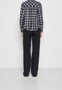 Navy plaid button-up shirt with gathered back, paired with dark cargo pants featuring side pockets and a straight fit, worn with white sneakers.