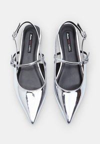 Hopeiset metalliset slingback-mokkasiinit, joissa on terävät varpaat, nilkkastrappi ja sileä pinta; musta sisäpohja merkkilabelilla.