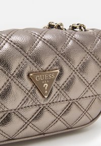 Metalická prošívaná kabelka ve stříbrném tónu s trojúhelníkovou zlatou logovou deskou. Disponuje řetízkem a texturovaným povrchem.