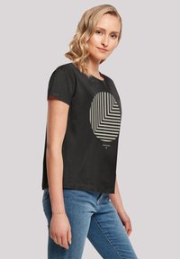 Schwarzes T-Shirt mit kurzen Ärmeln und einem gestreiften, kreisförmigen Grafikdesign in Creme. Der Stoff wirkt weich und leicht.