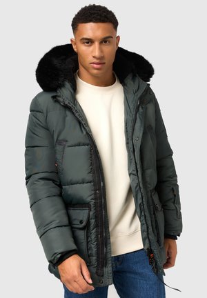 Grønne pufferjakke med en faux fur hætte, lynlås- og knaplukninger, sidelommer og ribbede manchetter. Båret over en lys sweatshirt.