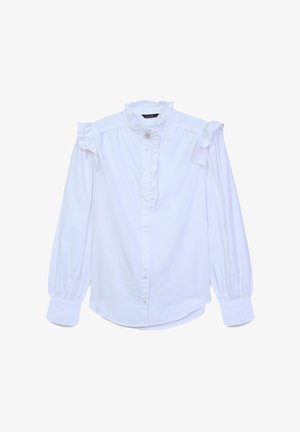 Blouse en coton blanc avec des épaules volantées, col montant et fermeture par bouton. Elle est dotée de manches longues avec des poignets froncés et d'un détail volanté à l'avant.