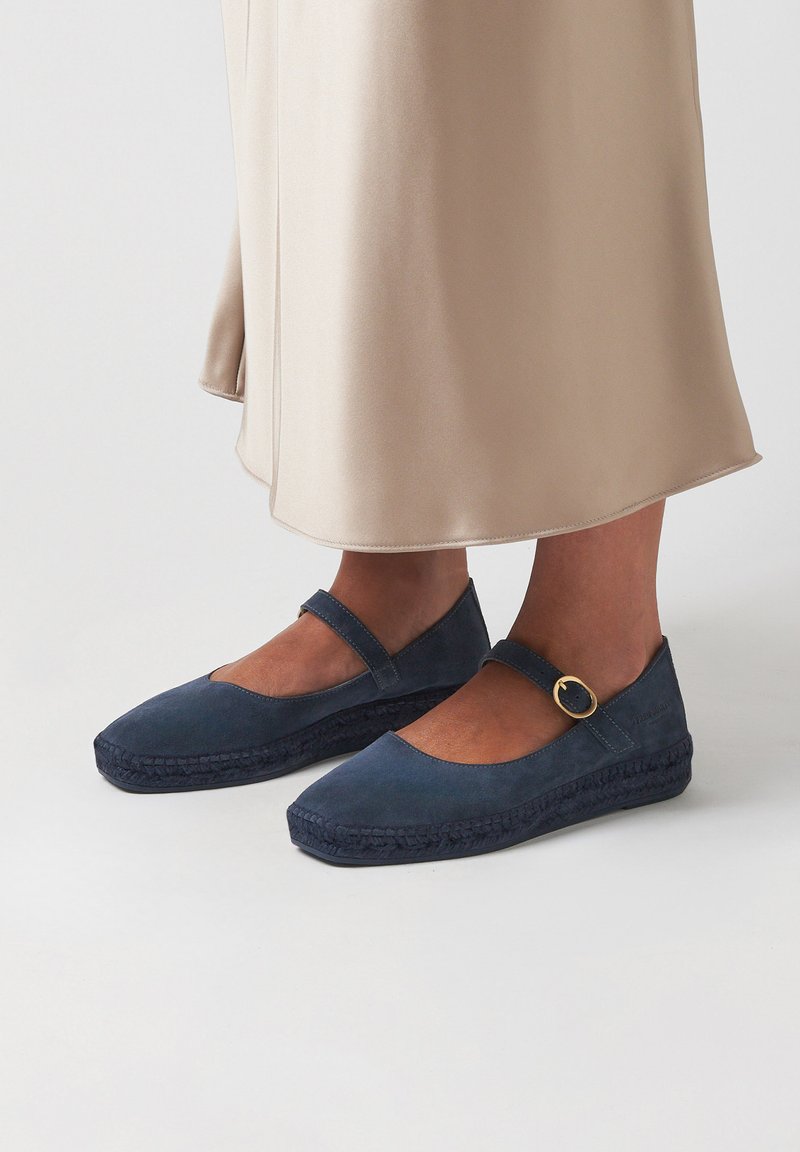 Tmavě modré espadrilky s plochým designem, zaoblenou špičkou, páskem se zlatou sponou a tkanými juty akcenty na podrážce.