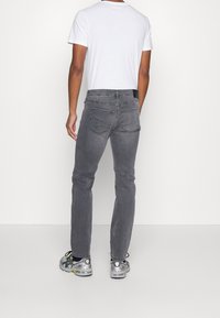 Vaqueros vaqueros grises de corte slim, con un diseño clásico de cinco bolsillos y costuras en contraste, usados con una camiseta blanca y zapatillas.