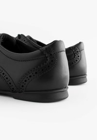 Chaussures en cuir noir avec un bout rond, des détails décoratifs perforés et une semelle en caoutchouc basse. La finition est lisse et mate.