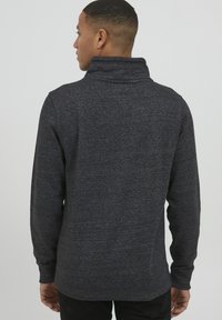 Pulover gri închis cu guler înalt, realizat dintr-un material texturat. Are mâneci lungi și un design ajustat, potrivit pentru ținute casual.