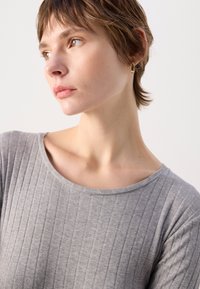 Grå ribbestrikket topp med bred utrigning og kortermede. Har en myk tekstur og subtile sømdetaljer. Nærbilde av utrigningen.