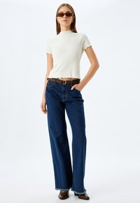 Hvid ribbet crop top med korte ærmer, parret med højhævet, bredbenet, mørkeblå denim jeans med flossede kanter. Brun bæltet medfølger.