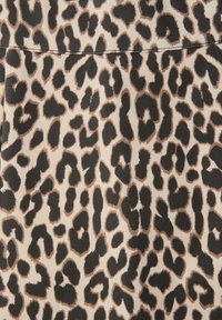 Tissu beige avec un motif léopard irrégulier noir et marron, et une couture horizontale visible près du haut.
