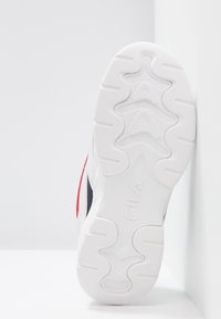Suela de zapatilla deportiva blanca con goma texturizada para agarre, que presenta un diseño elevado y la marca Fila en la suela. Acentos en rojo y azul marino visibles.