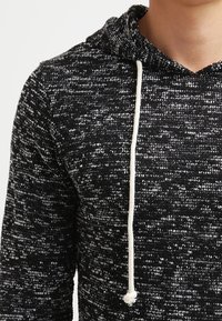 Hoodie lavorato a maglia bianco e nero con un motivo testurizzato, dotato di cordino in bianco sporco e una vestibilità rilassata attorno al collo.