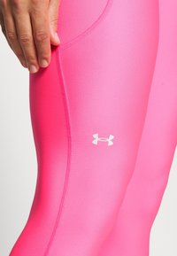 Barevně sladěné sportovní legíny v jasně růžové barvě, s hladkou texturou a bílým logem značky. Viditelné boční švy.