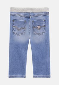 Pantalones de mezclilla azul claro con una cinturilla acanalada gris, que cuentan con dos bolsillos traseros con detalles de costura y un parche con el logo.