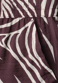 Gros plan d’un tissu rayé zèbre violet et blanc, montrant des coutures surpiquées et une ceinture élastique froncée.