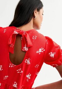 Rotes Blumenkleid aus strukturiertem Stoff mit Puffärmeln, einem Schlüsselloch-Rücken mit Schleife und einer gerafften Taillenlinie.