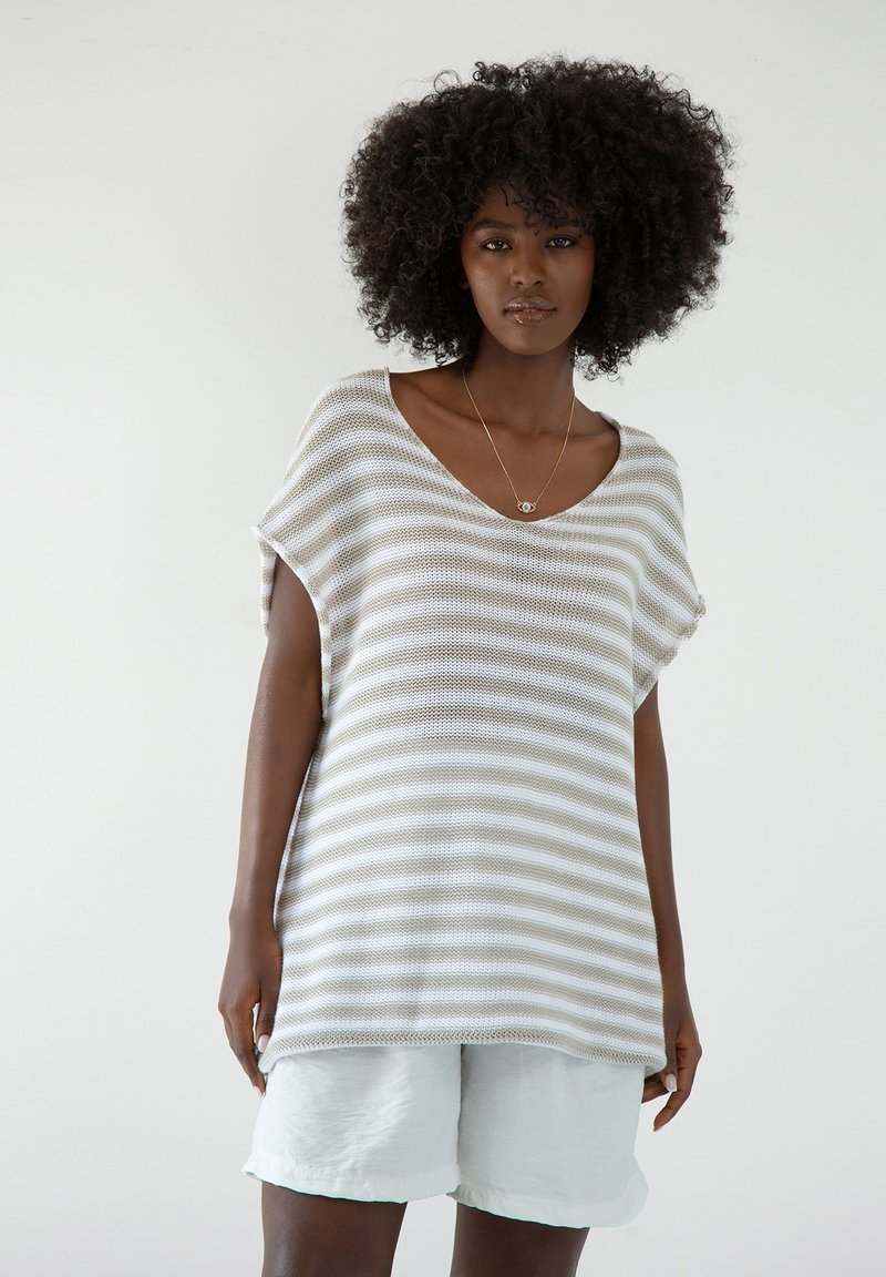 Pasiasty, oversize sweter w jasnym beżu i bieli, z głębokim dekoltem w kształcie V i krótkimi rękawami, w zestawie z jasnoniebieskimi szortami.