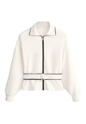 Bela jakna na zadrgo s črnim obrobami na ovratniku, zadrgi in robu, s pasom v enakem slogu v pasu ter dolgimi rokavi z manšetami.