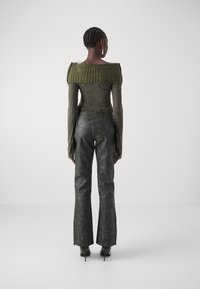 Olivgrön topp med texturerad rand på axeln, i kombination med svarta läderbyxor med utsvängda ben, som har spikade midjeband och dragkedjeändar.
