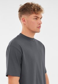 Ciemnoszara, krótki rękaw, t-shirt z okrągłym dekoltem. Miękka tekstura, luźny krój, brak widocznych wzorów lub logo. Prosty i uniwersalny design.