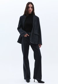 Černý džínový oversized blazer a odpovídající rozšířené kalhoty s bílými švy. Nošeno s černým rolákem a černými vysokými botami na podpatku.