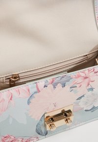 Handtasche mit Blumenmuster, metallischem Verschluss, hellblauem Äußeren und beigem Innenfutter mit einer Reißverschlusstasche zur Aufbewahrung.