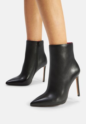 Bottines en cuir noir avec une finition brillante, bouts pointus et talons aiguille fins, dotées d'une fermeture éclair sur le côté.
