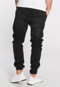 Pantalones jogger de mezclilla negra con un ajuste slim, con bolsillos traseros y tobillos ajustados, combinados con zapatillas deportivas blancas.