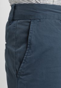 Shorts en coton bleu marine avec une texture лisse, une coupe droite, des passants de ceinture et des poches latérales. Le tissu a un léger éclat.