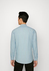 Lange mouw overhemd in lichtblauw met witte verticale strepen. Zachte textuur, knoopmanchetten, afgeronde zoom en een klassiek kraagontwerp.