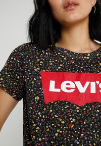 Camiseta negra con un estampado floral que presenta pequeñas flores multicolores, cuello redondo y un destacado logotipo rojo de Levi's en el pecho.