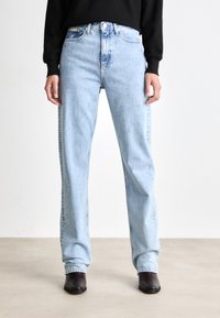 Jeans de mezclilla de tiro alto en azul claro, con piernas rectas, que cuentan con un cierre delantero de botón y un diseño tradicional de cinco bolsillos. Textura suave.
