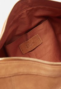 Intérieur d'un sac en suède marron montrant une poche en tissu et une étiquette de marque ZIGN cousue à l'intérieur du compartiment principal.
