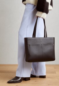 Sort struktureret faux læder tote bag med to hanke, der har en glat tekstur, diskrete sting og en forlomma med gyldne detaljer.