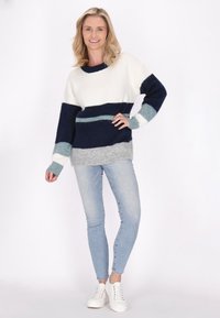 Pulover tricotat cu dungi bleumarin, alb și bleu deschis; mâneci lungi; croială lejeră; margine de jos gri; asortat cu blugi bleu deschis și adidași albi.