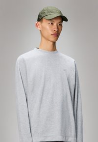 Sweatshirt cinza com mangas longas e decote redondo, apresentando um logo subtil no peito. Combinado com um boné verde claro.